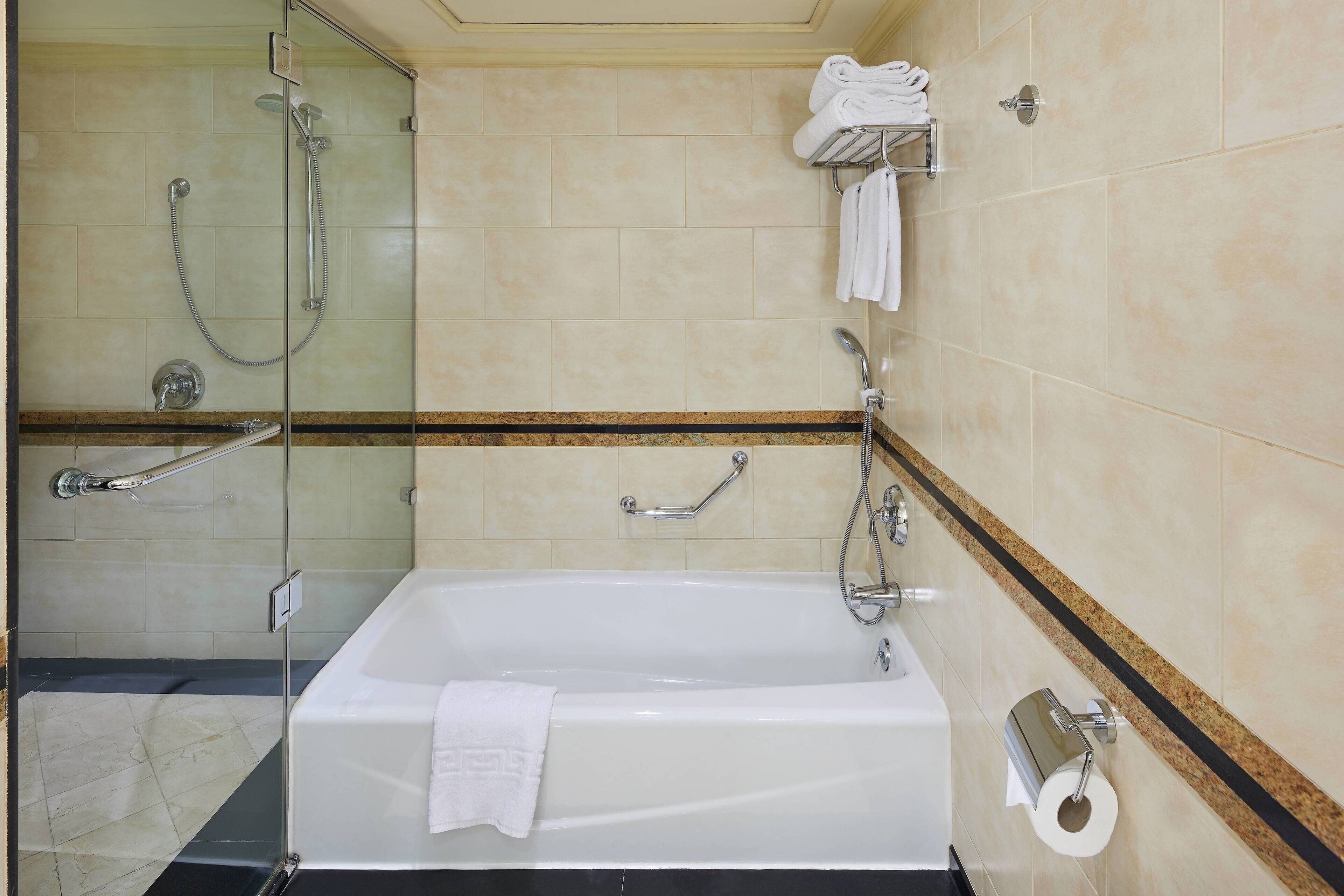 A modern bathroom with a glass-enclosed shower, a white bathtub, and a towel rack with folded towels.