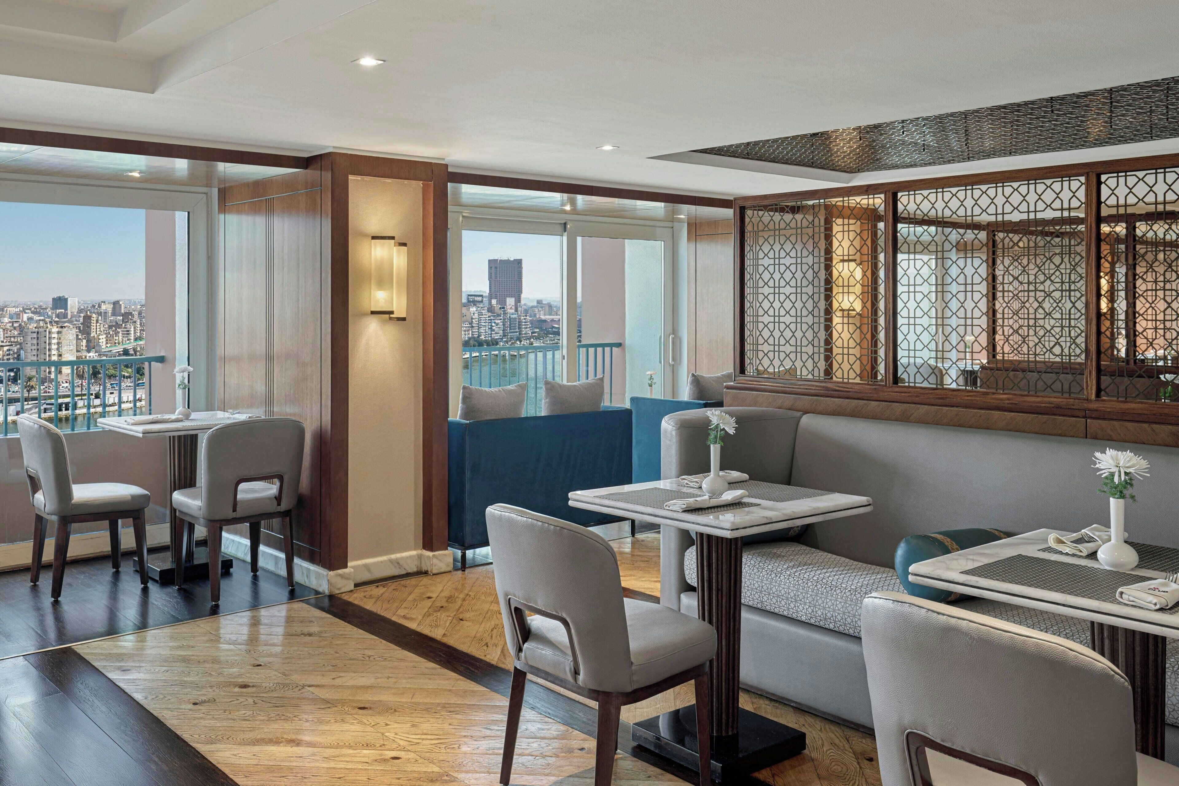 Una habitación de hotel moderna con vistas a la ciudad, un balcón y un área de comedor con mesas y sillas.