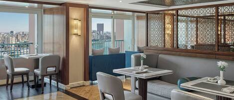 Una habitación de hotel moderna con vistas a la ciudad, un balcón y un área de comedor con mesas y sillas.