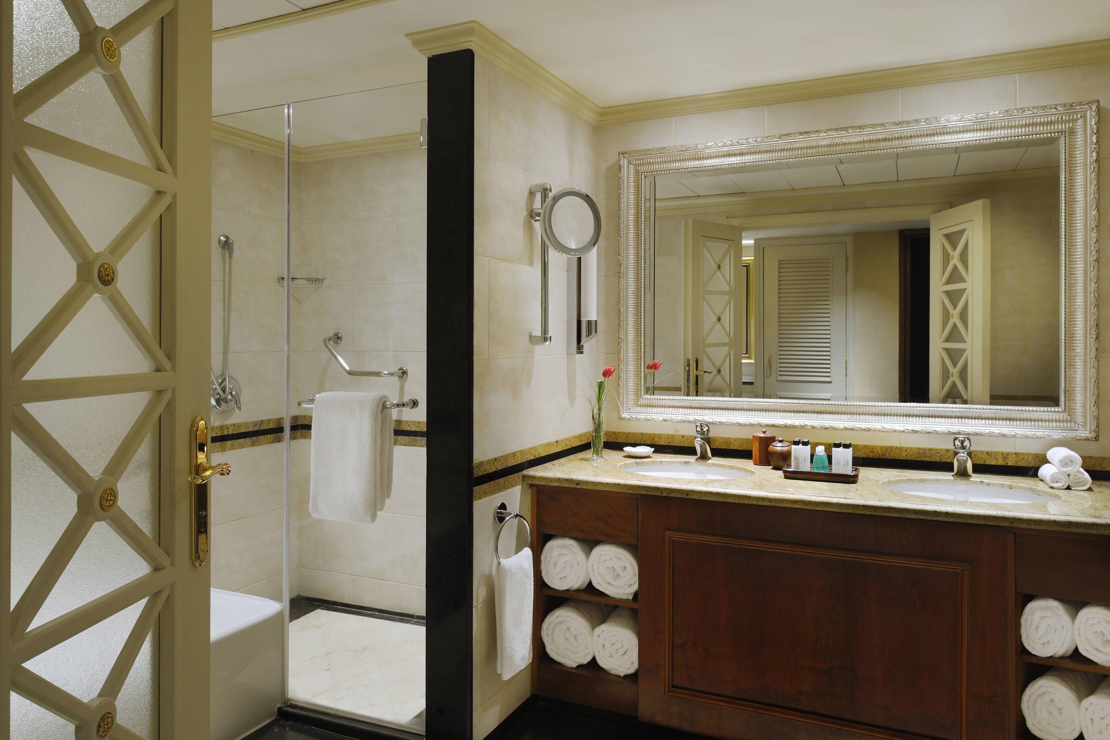 A bathroom with a glass shower enclosure, a vanity with a large mirror, and multiple towels neatly stacked.