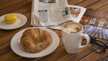 Un croissant su un piatto, una tazza di caffè, un paio di occhiali e un giornale su un tavolo di legno.