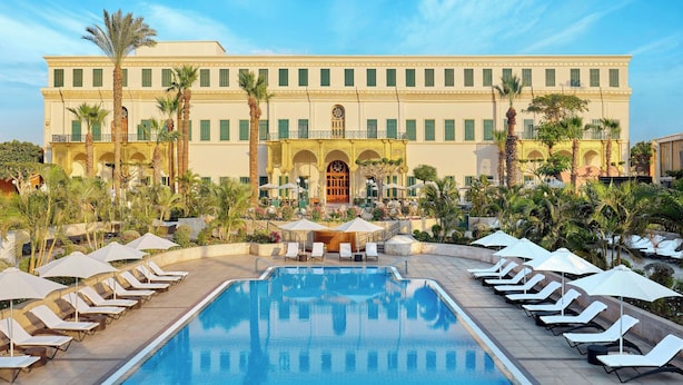 A hotel with a pool, sun loungers, and palm trees.