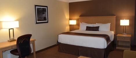 A hotel room with a bed, desk, chair, and bedside table.