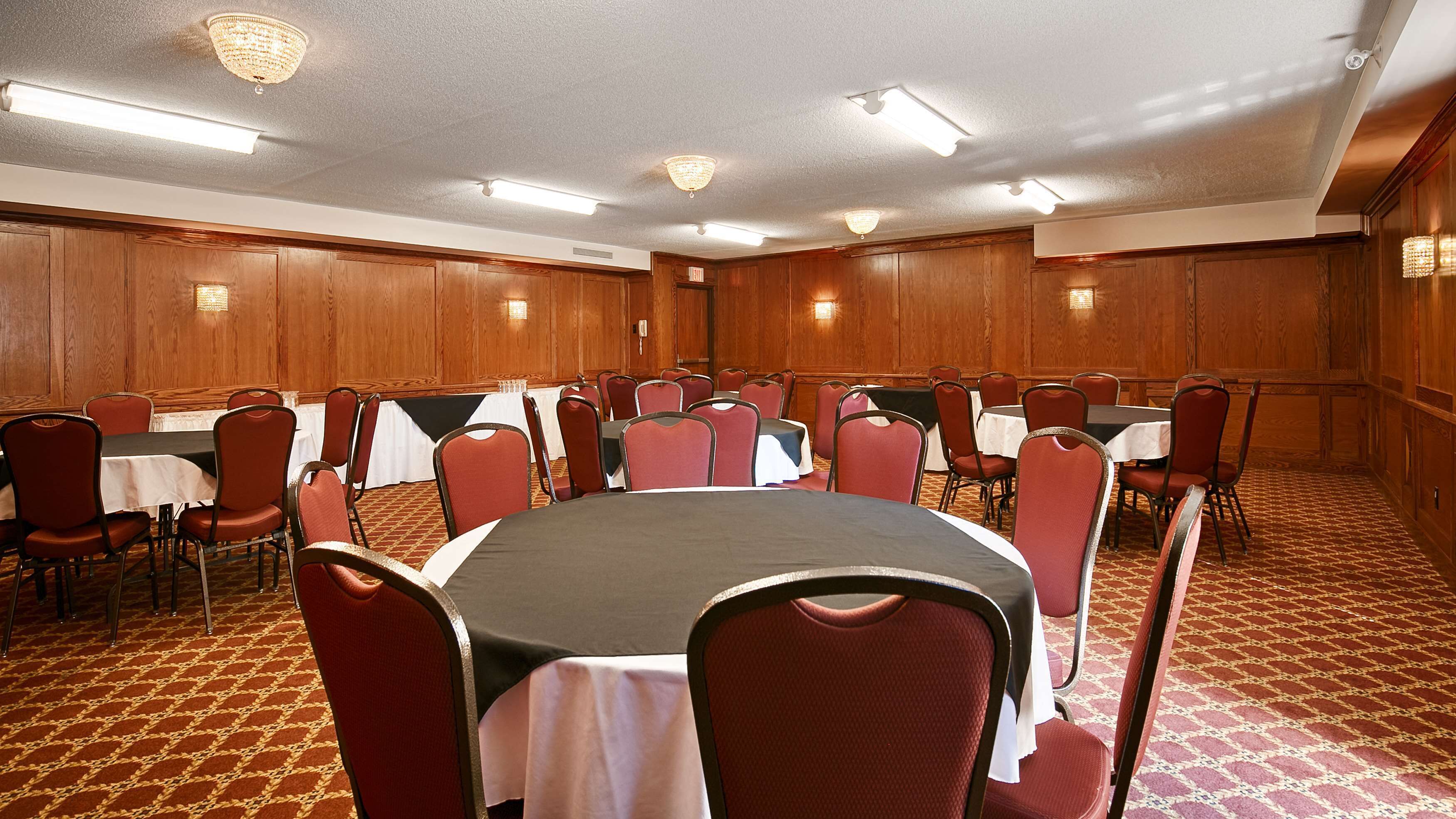 A conference room with round tables and red chairs, wooden paneling on the walls, and patterned carpet.