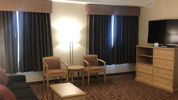 A hotel room with a sofa, two armchairs, a small table, a TV, and a ceiling fan.