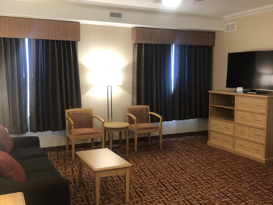 A hotel room with a sofa, two armchairs, a small table, a TV, and a ceiling fan.