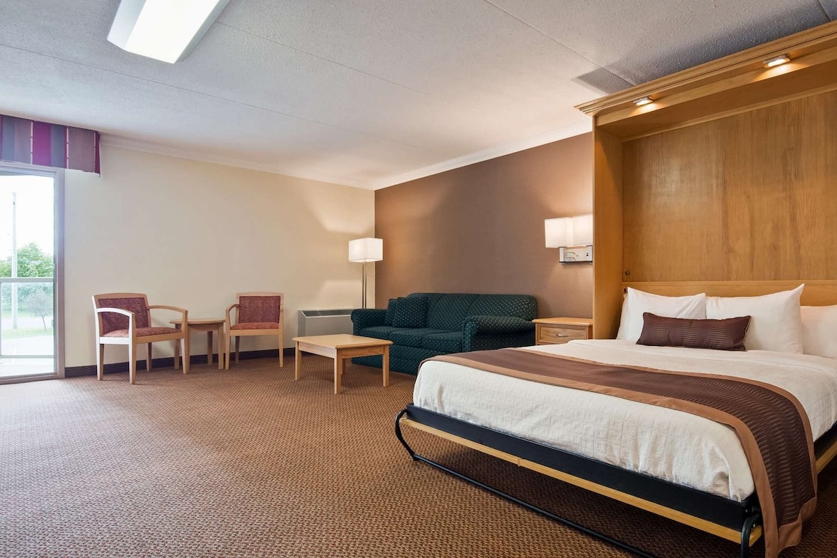 A hotel room with a bed, a desk, a chair, a sofa, and a lamp.
