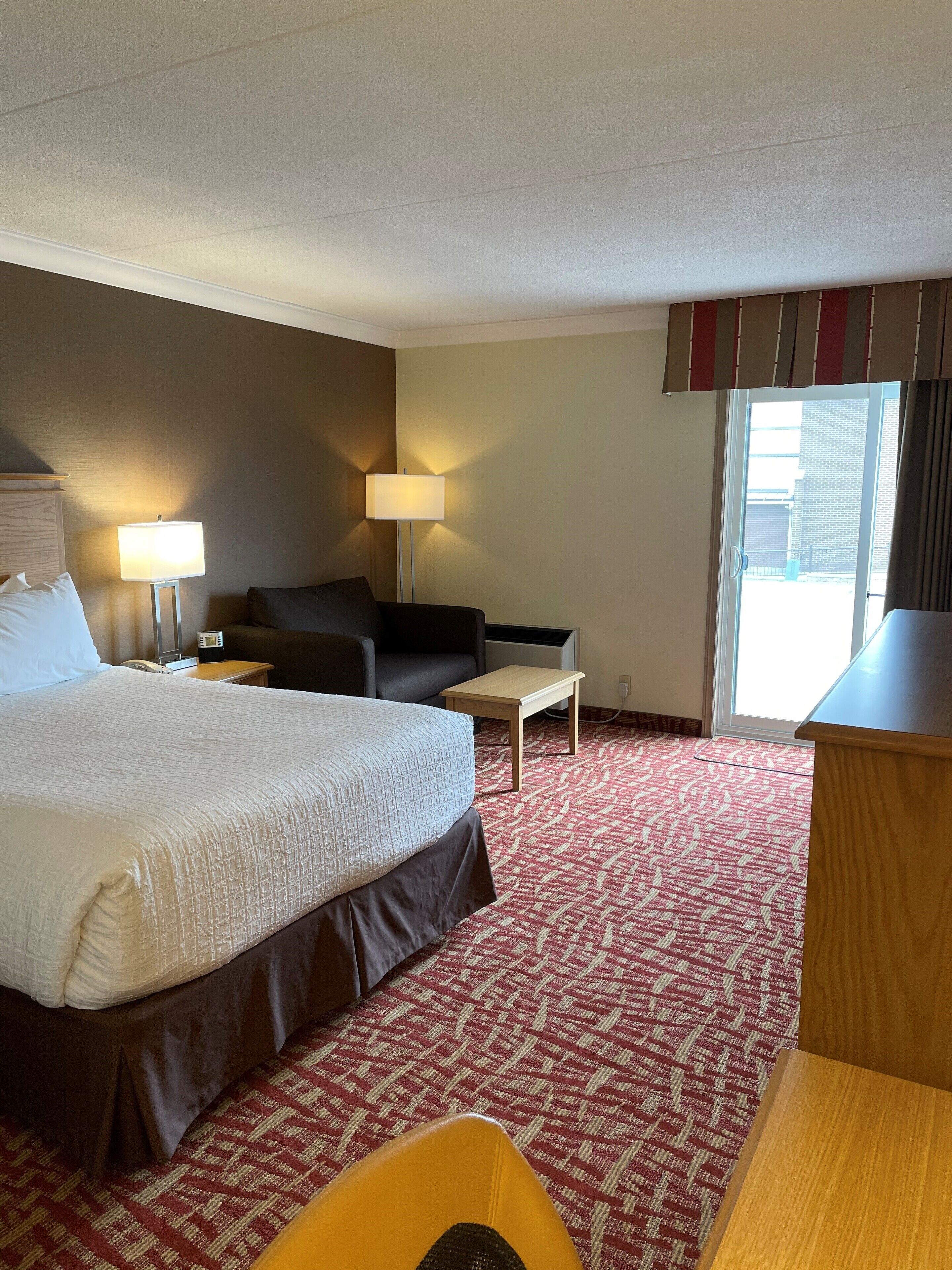 A hotel room with a large bed, a desk, a chair, a sofa, and two lamps.