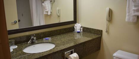 A bathroom with a granite countertop sink, a mirror, a toilet, and a shower area.