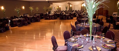 A banquet hall with round tables set for dining, draped with white curtains, and adorned with tall floral arrangements.