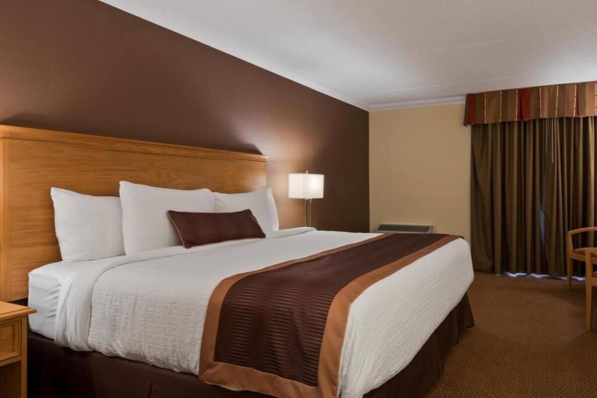 A hotel room with a large bed, a wooden headboard, a nightstand, a lamp, and a chair.