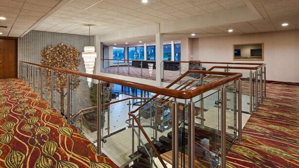A hotel lobby with a glass railing, a patterned carpet, and a chandelier. - Best Western Plus Cobourg Inn & Convention Centre (Cobourg)
