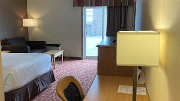 A hotel room with a bed, a desk with a lamp, a chair, and a view of the outside.