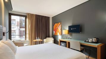 Una habitación de hotel con cama, escritorio, silla, televisor y ventana con cortinas.