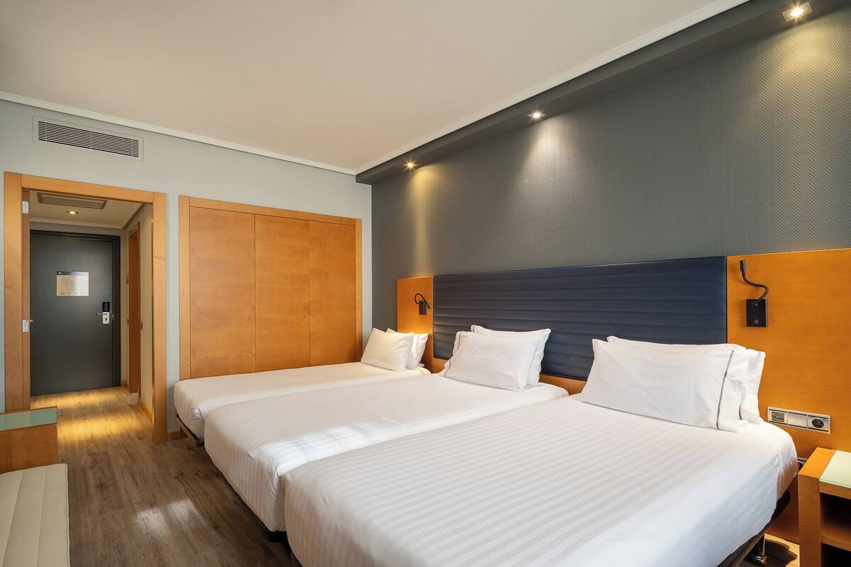 Hotellihuone, jossa on kaksi sänkyä, puinen vaatekaappi ja moderni sängynpääty.
