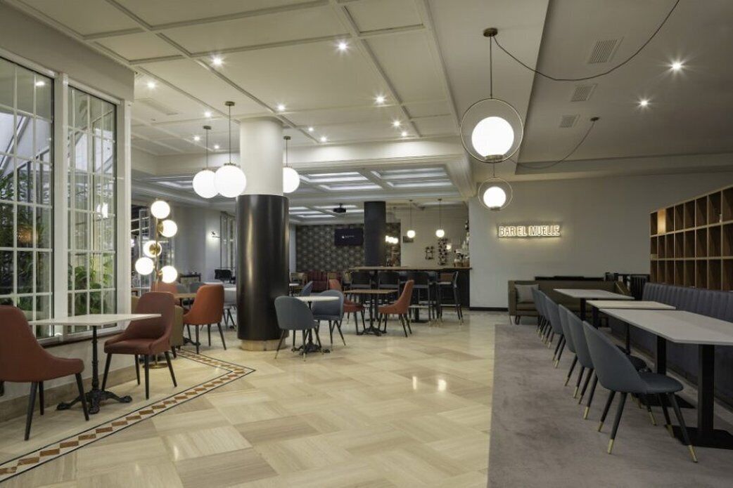 A modern restaurant with a high ceiling, pendant lighting, and a mix of seating arrangements.