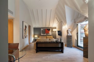 Una camera d'albergo moderna con divano, tavolino, televisore e opere d'arte alle pareti.