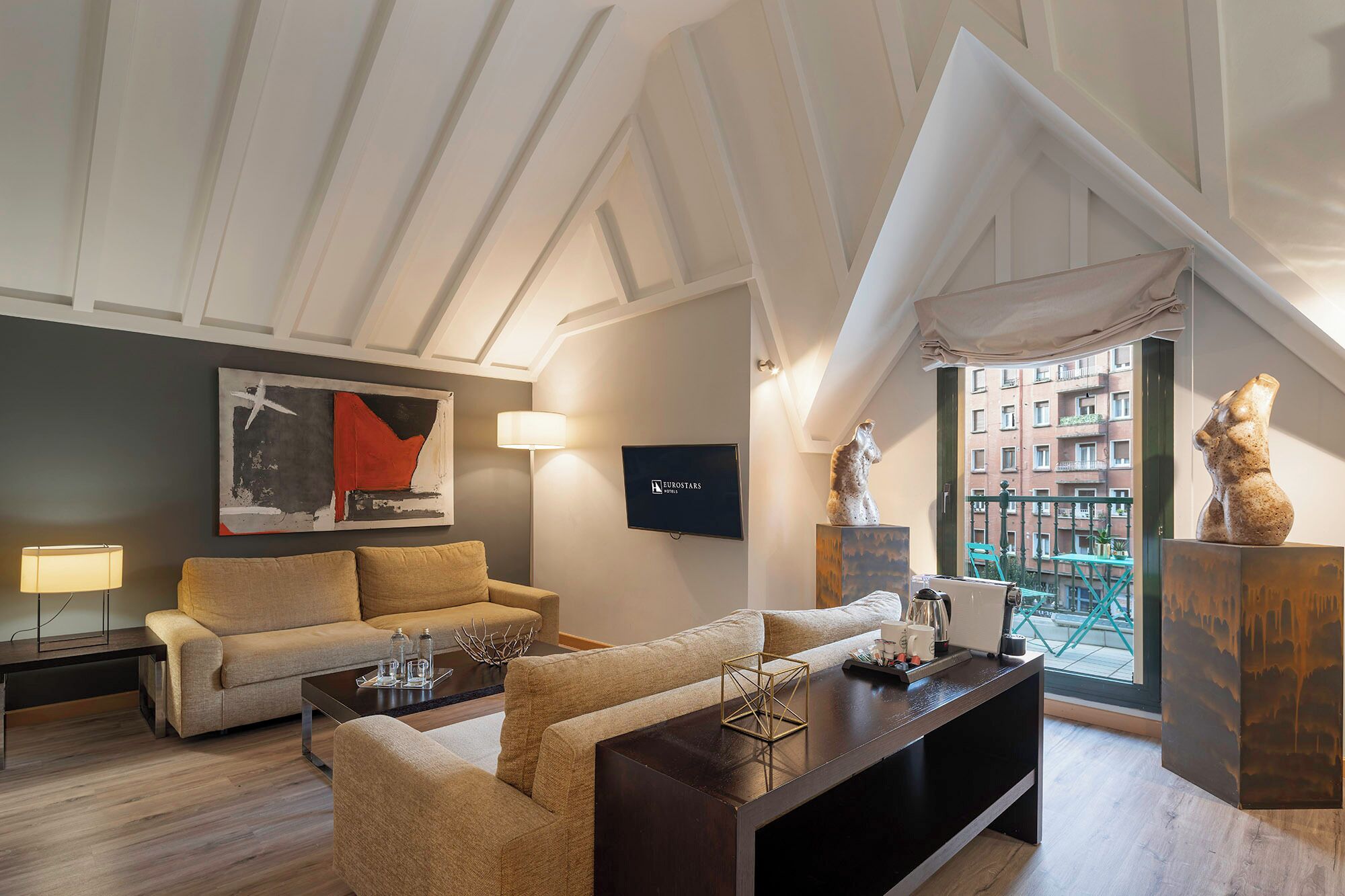 A modern living room with a high ceiling, a sofa, a coffee table, a TV, and artwork.