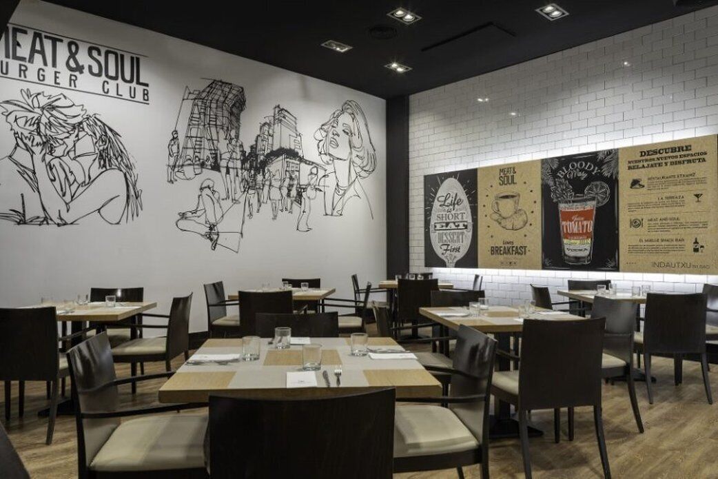 Un interno ristorante con tavoli e sedie, un murale sulla parete e bacheche con il menu.