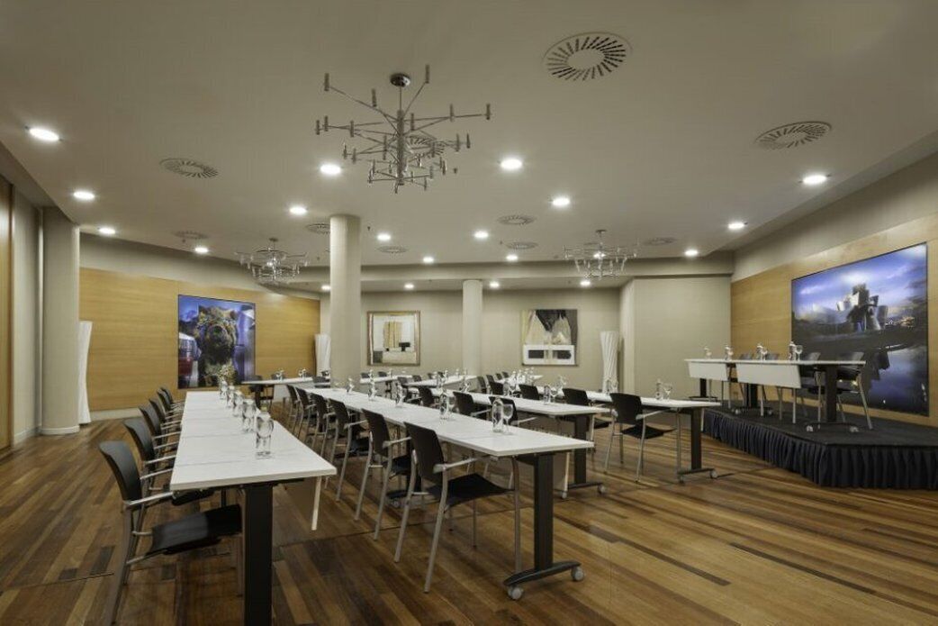 Una sala de conferències amb taules llargues, cadires i una zona d'escenari.
