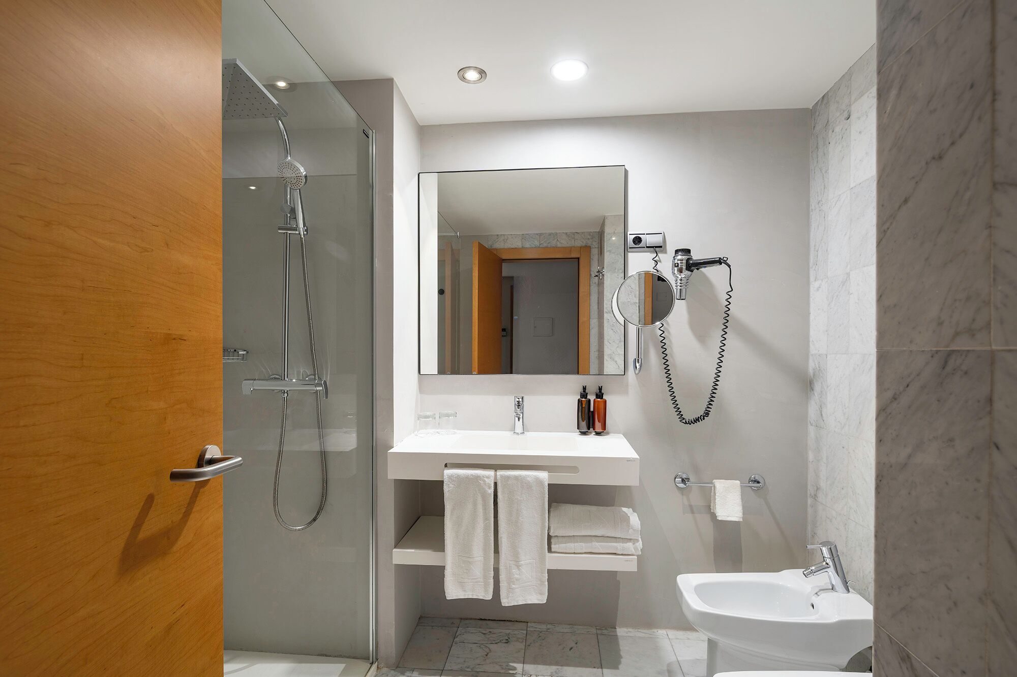 Un baño moderno con ducha envuelta en vidrio, tocador con espejo y lavamanos.