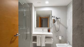 Un baño moderno con ducha envuelta en vidrio, tocador con espejo y lavamanos.