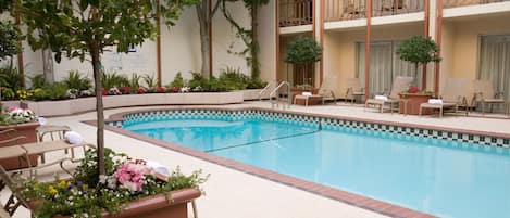 A hotel pool area with lounge chairs, a small pool, and a balcony with railings.