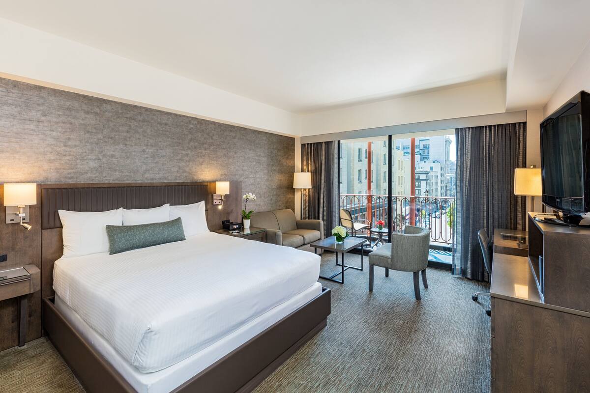 Habitación de hotel con una cama grande, un escritorio, una silla, una mesita y un televisor.