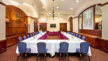 A conference room with a long table, blue chairs, a chandelier, wooden paneling, and a large mirror.