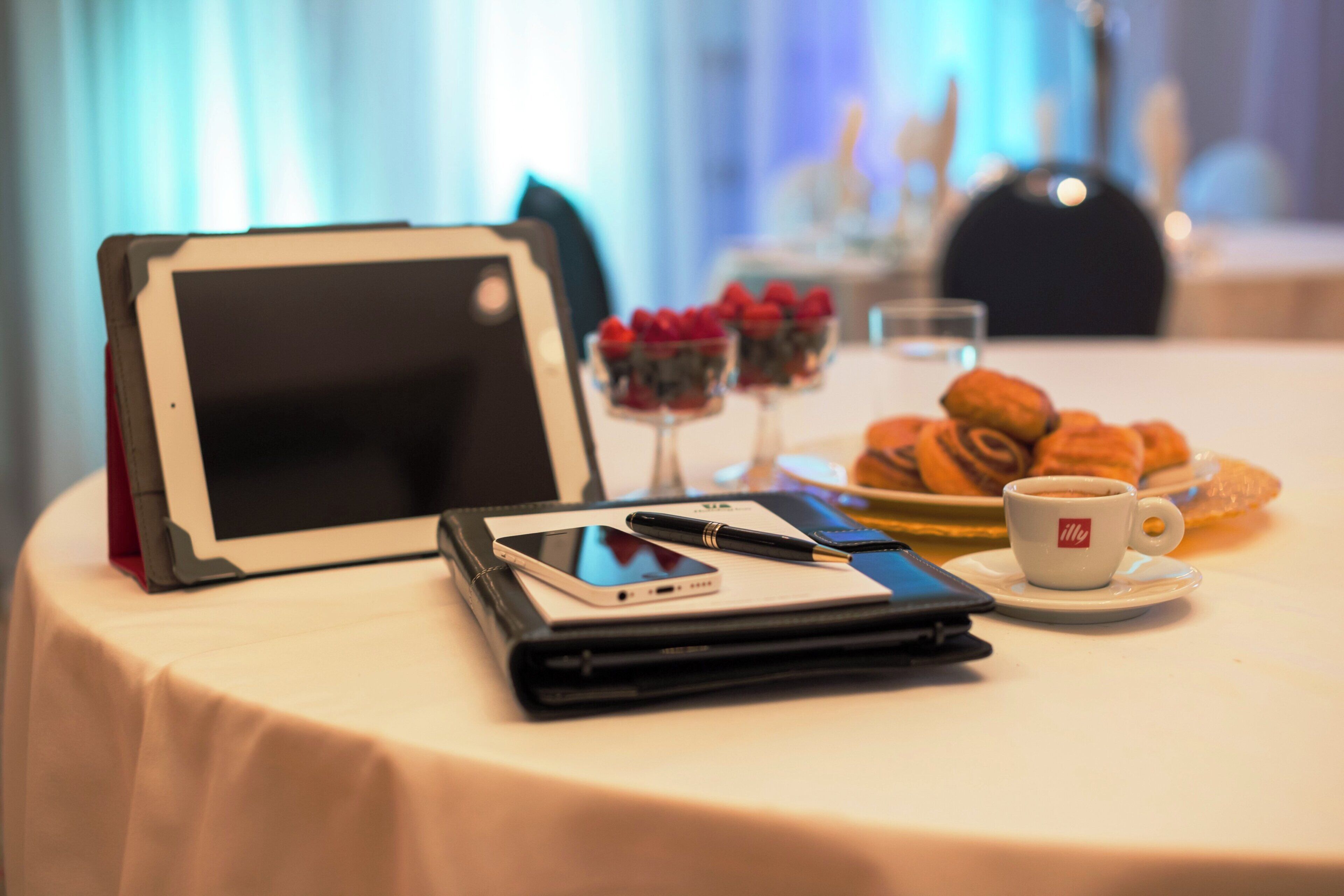 A table with a tablet, smartphone, pen, notebook, and a cup of coffee.