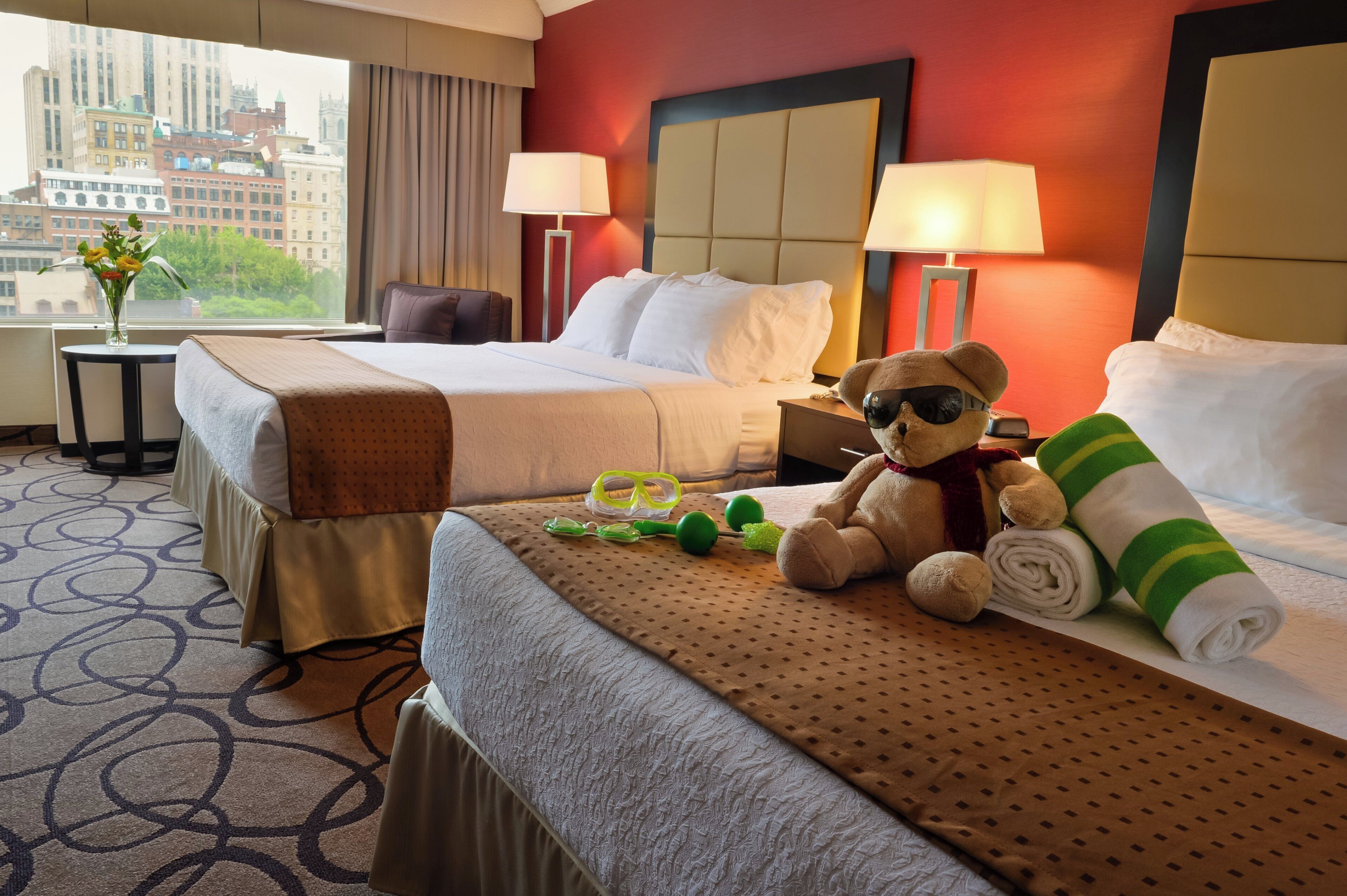 A hotel room with two beds, a view of the city, and a teddy bear on one bed.