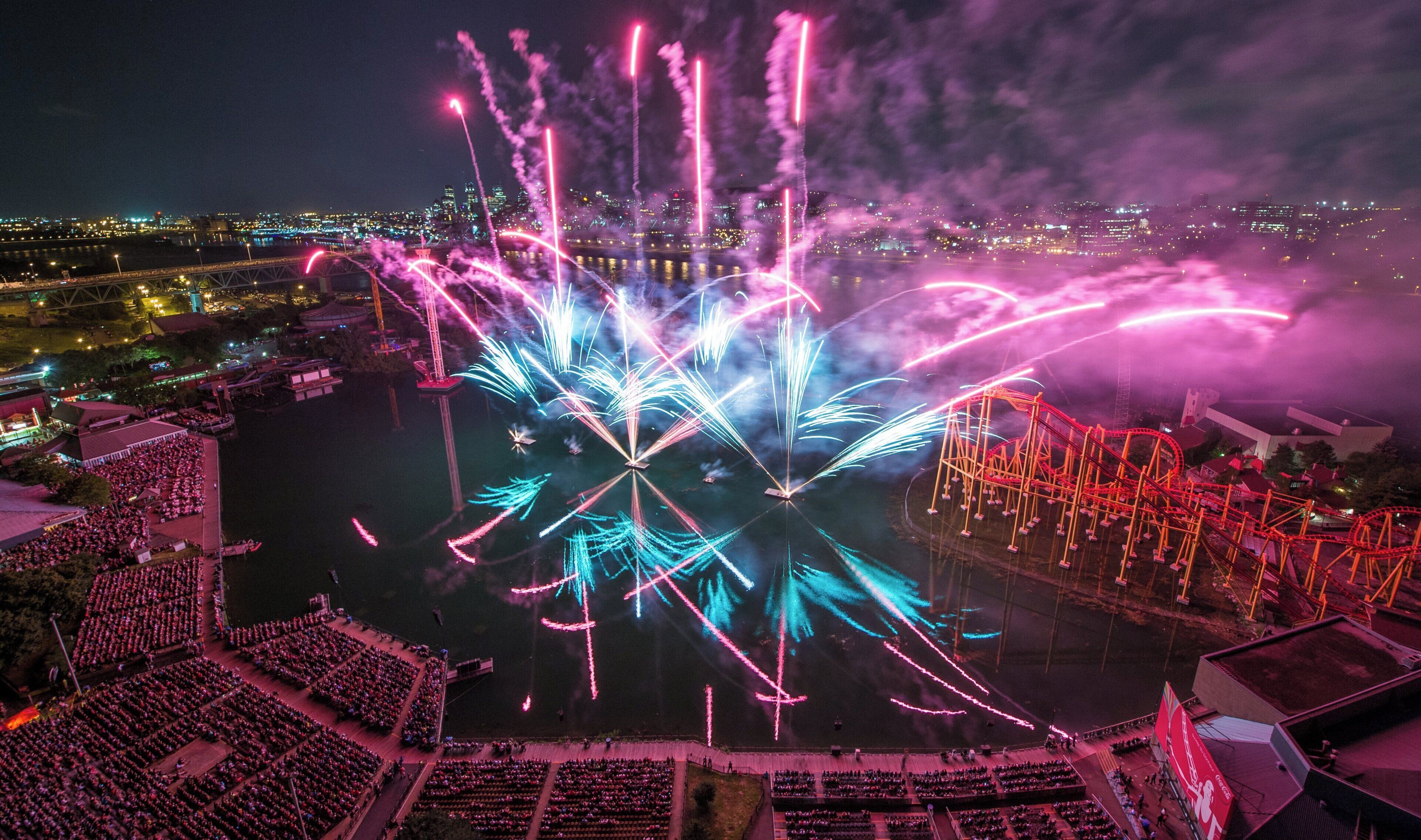 A large outdoor venue with a stage, seating, and a roller coaster.