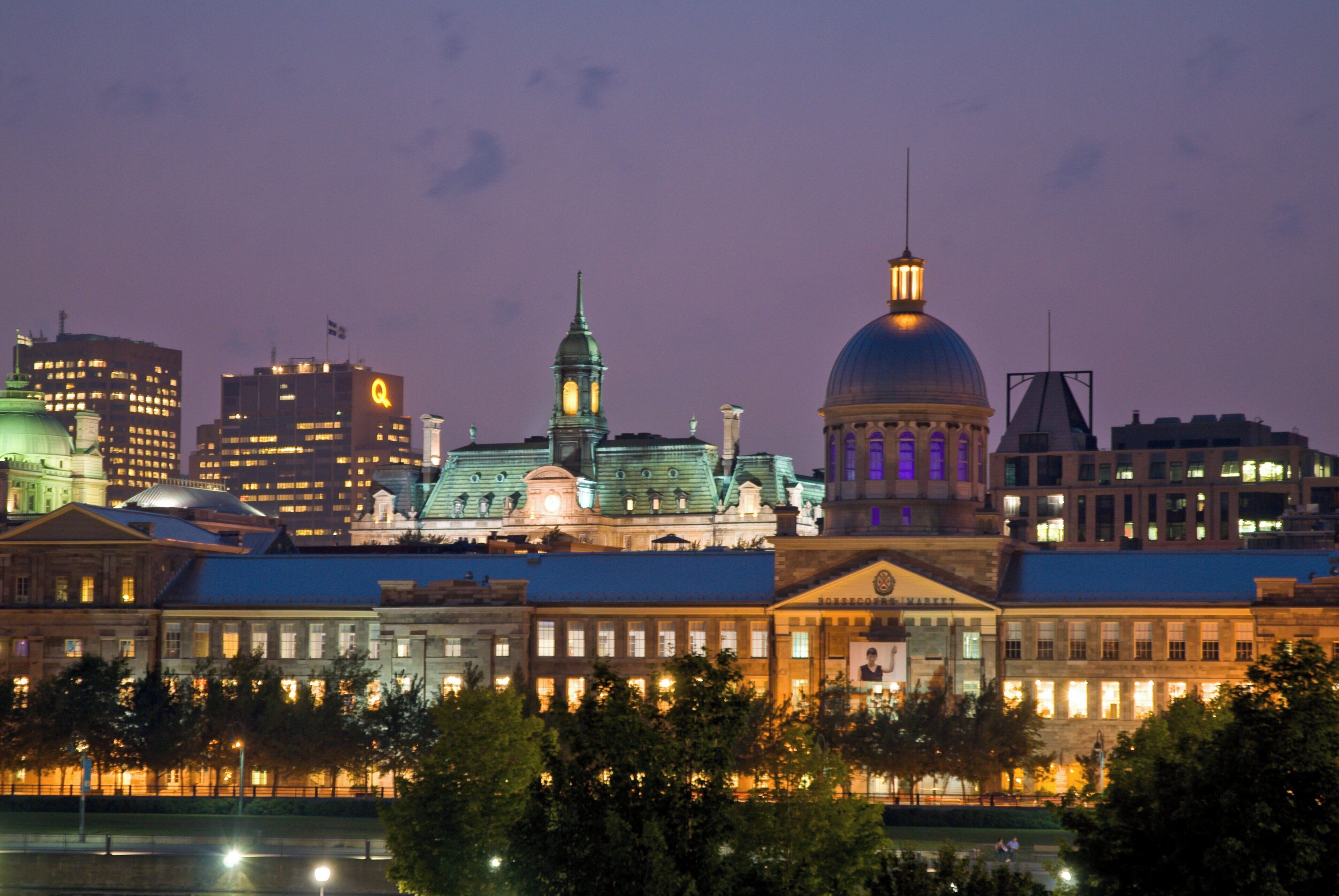 A city skyline at dusk with illuminated buildings and a prominent dome structure.