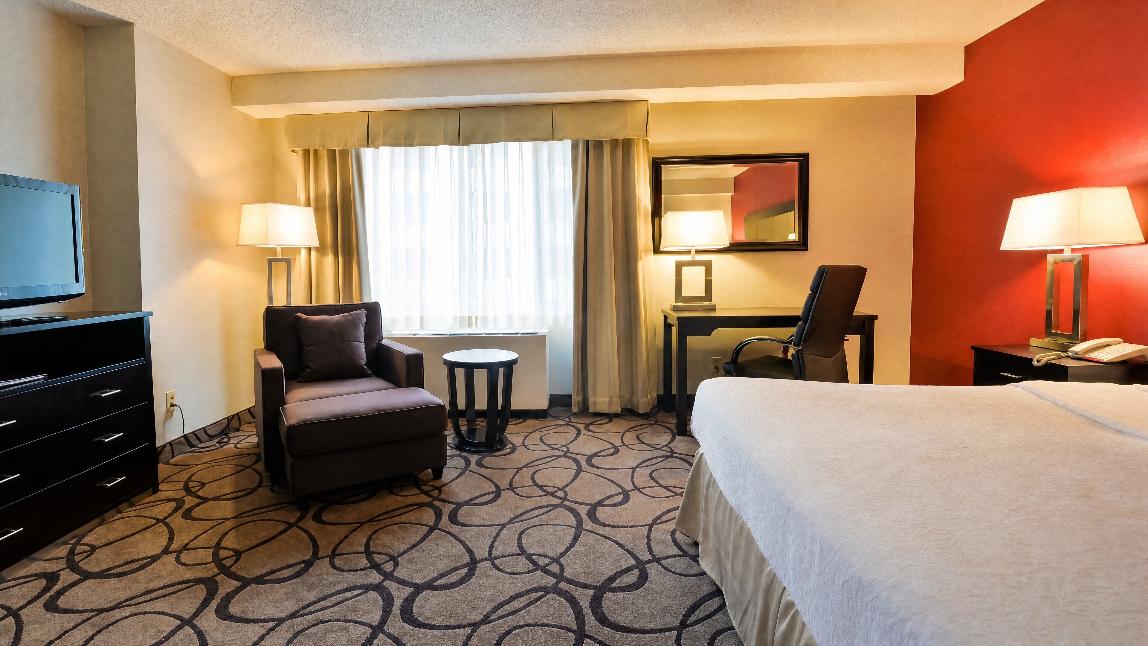 A hotel room with a bed, a desk, a chair, a television, and a telephone.