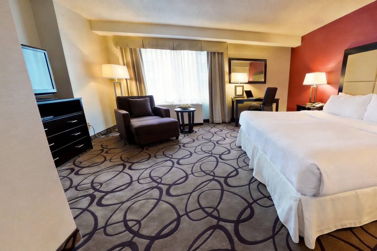 A hotel room with a bed, a desk, a chair, a TV, and a dresser.