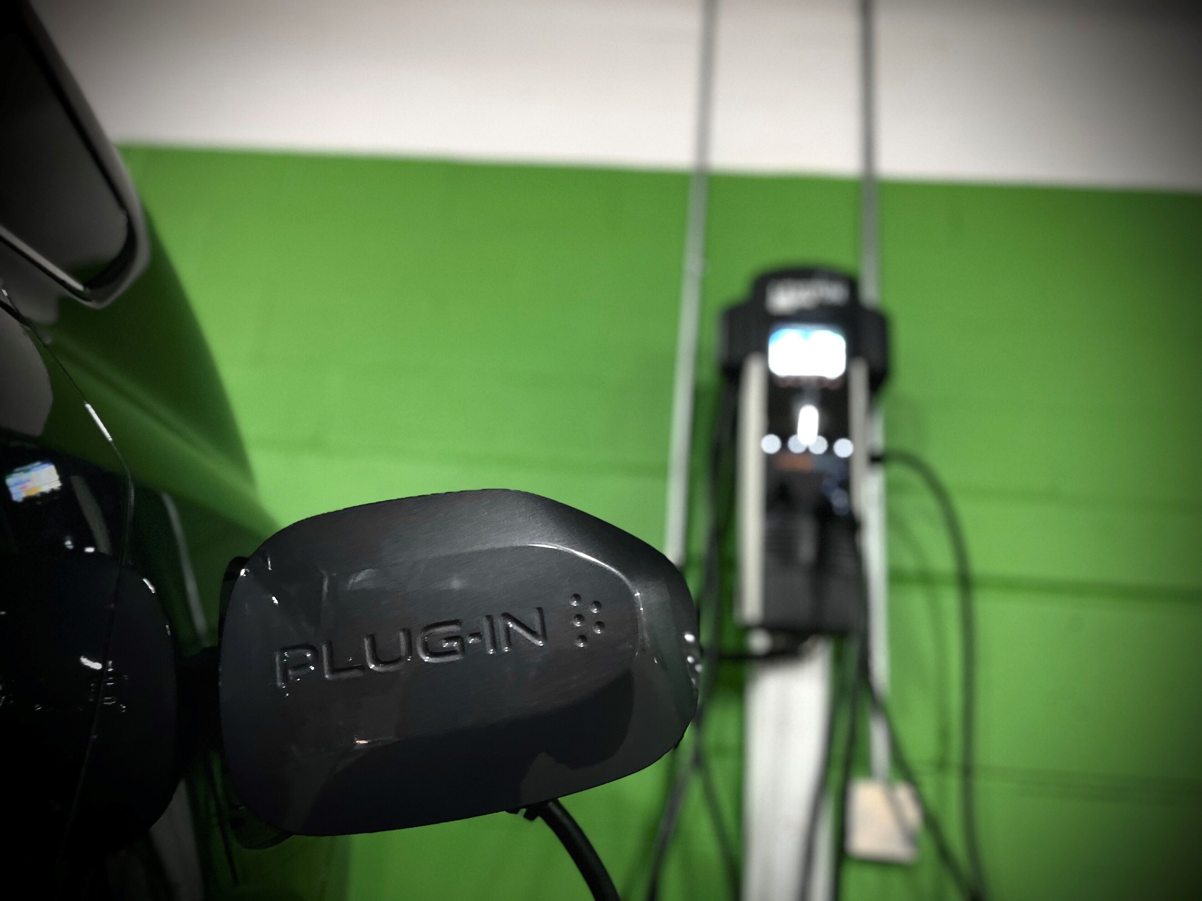 A close-up of a black object with the text "PLUGIN" on it, connected to a green wall.