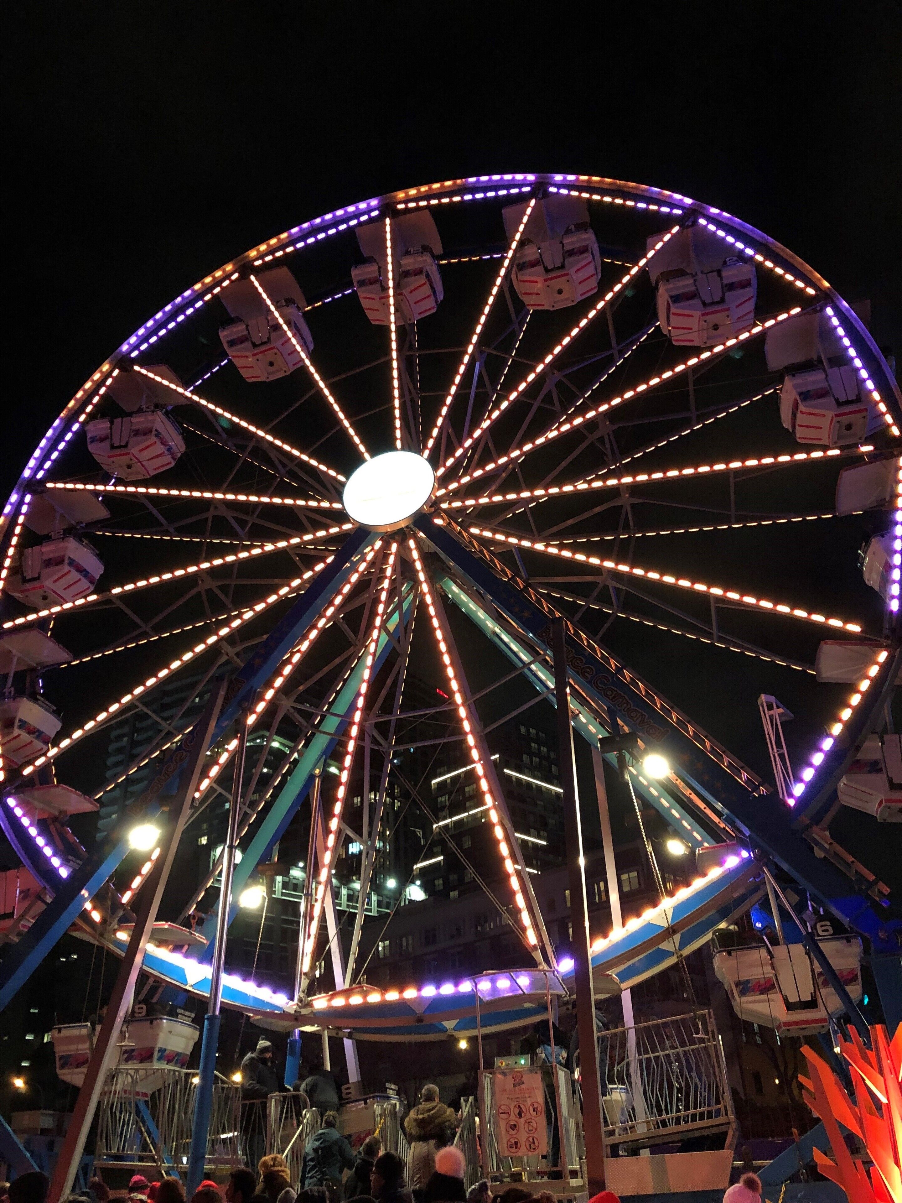 Ein Riesenrad mit mehreren Gondeln, beleuchtet durch farbige Lichter, und einem Metallgerüst, das die Konstruktion trägt.