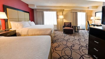 A hotel room with two beds, a desk, a chair, and a TV.
