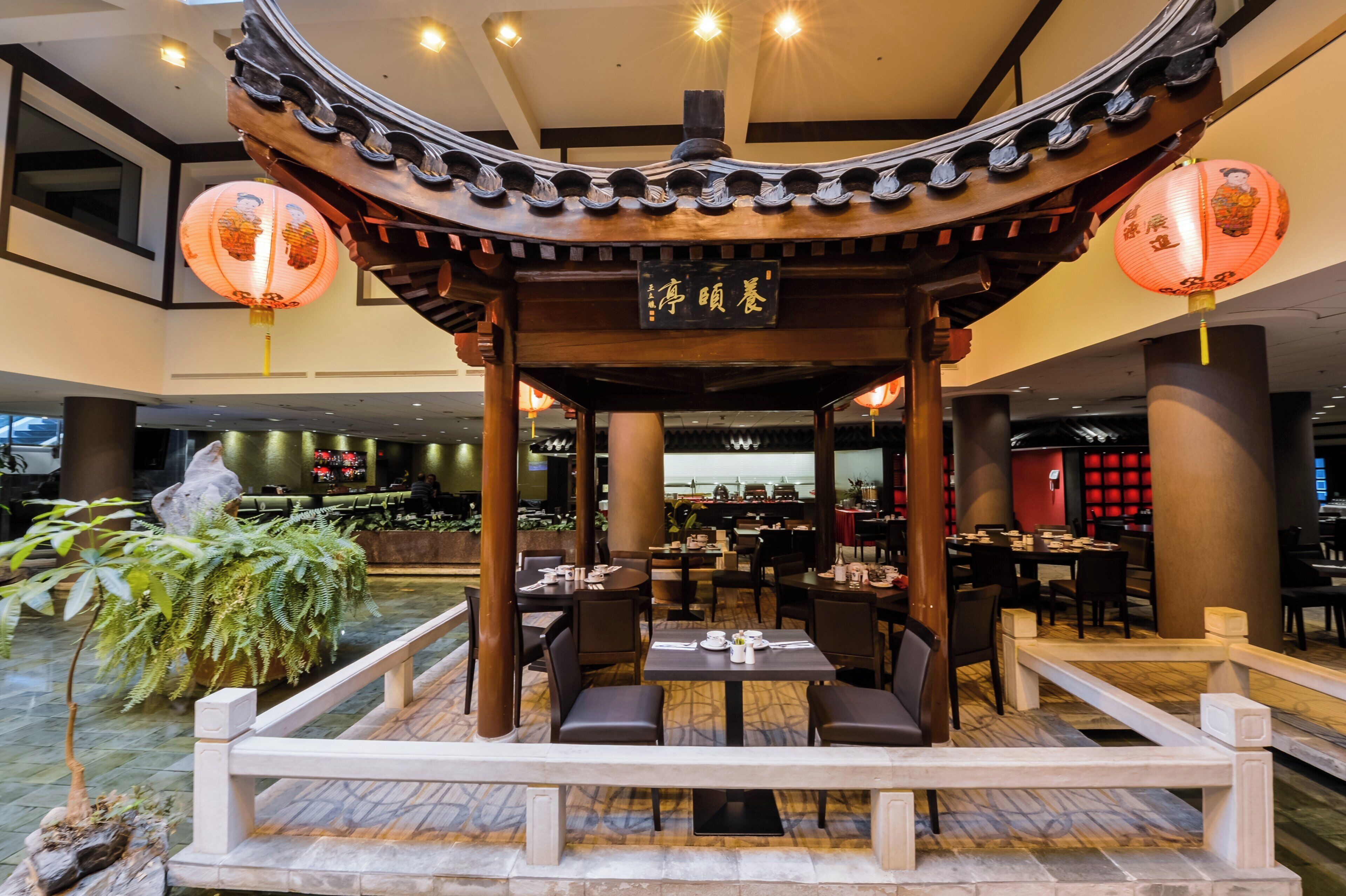 A traditional Chinese pavilion with tables and chairs, surrounded by indoor plants and a bar area.