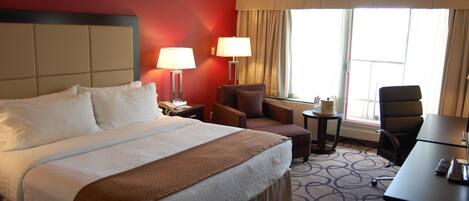 Una habitación de hotel con una cama grande, dos sillones, un escritorio y una mesita.
