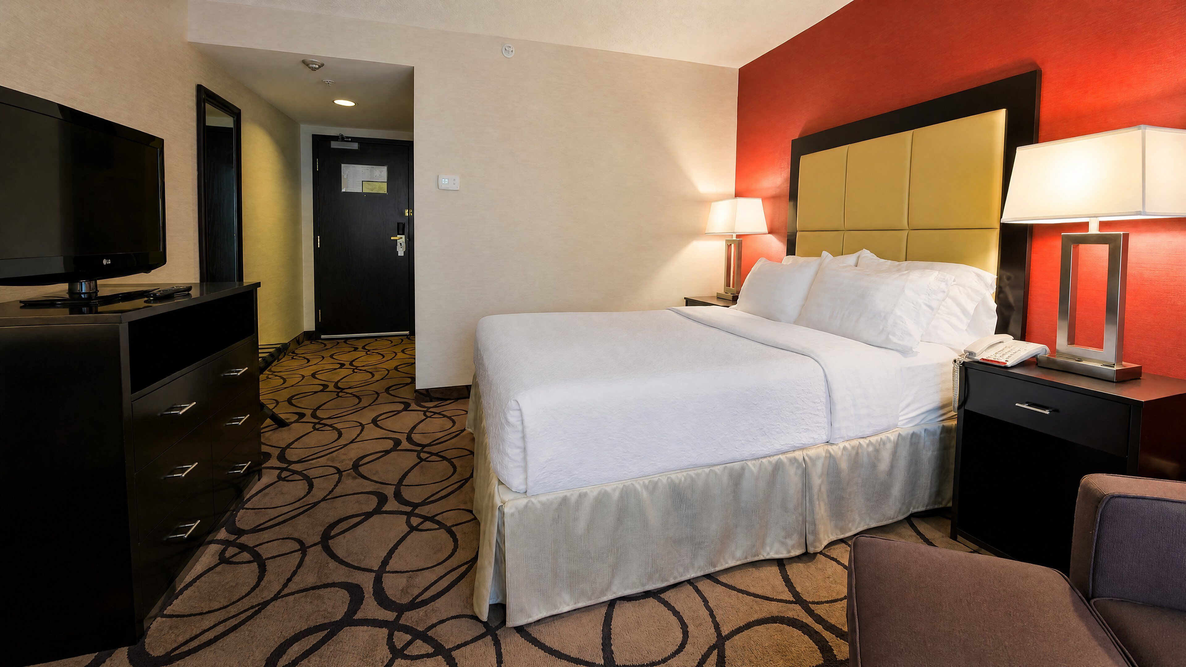 A hotel room with a bed, a TV, a desk, and a chair.