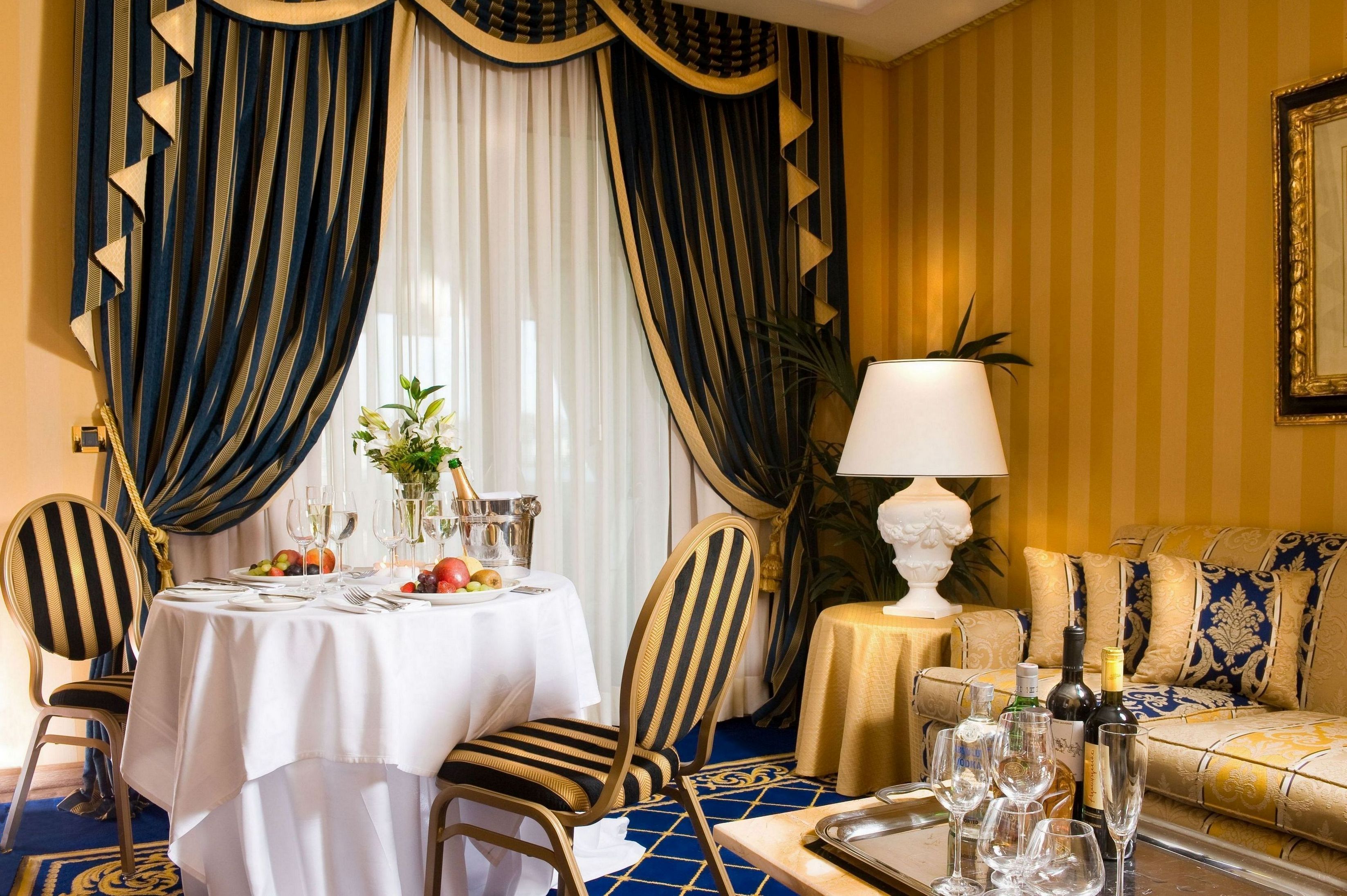 A dining area with a table set for two, a sofa, and a lamp.