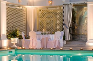 Ein Essbereich am Pool mit einem Tisch für zwei Personen, umgeben von weißen Stühlen, Kerzen und einem Blumentopf.