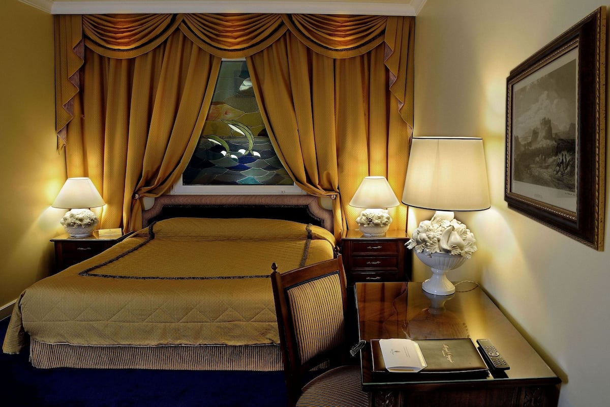 A hotel room with a large bed, two bedside tables with lamps, a framed picture on the wall, and a window with curtains.