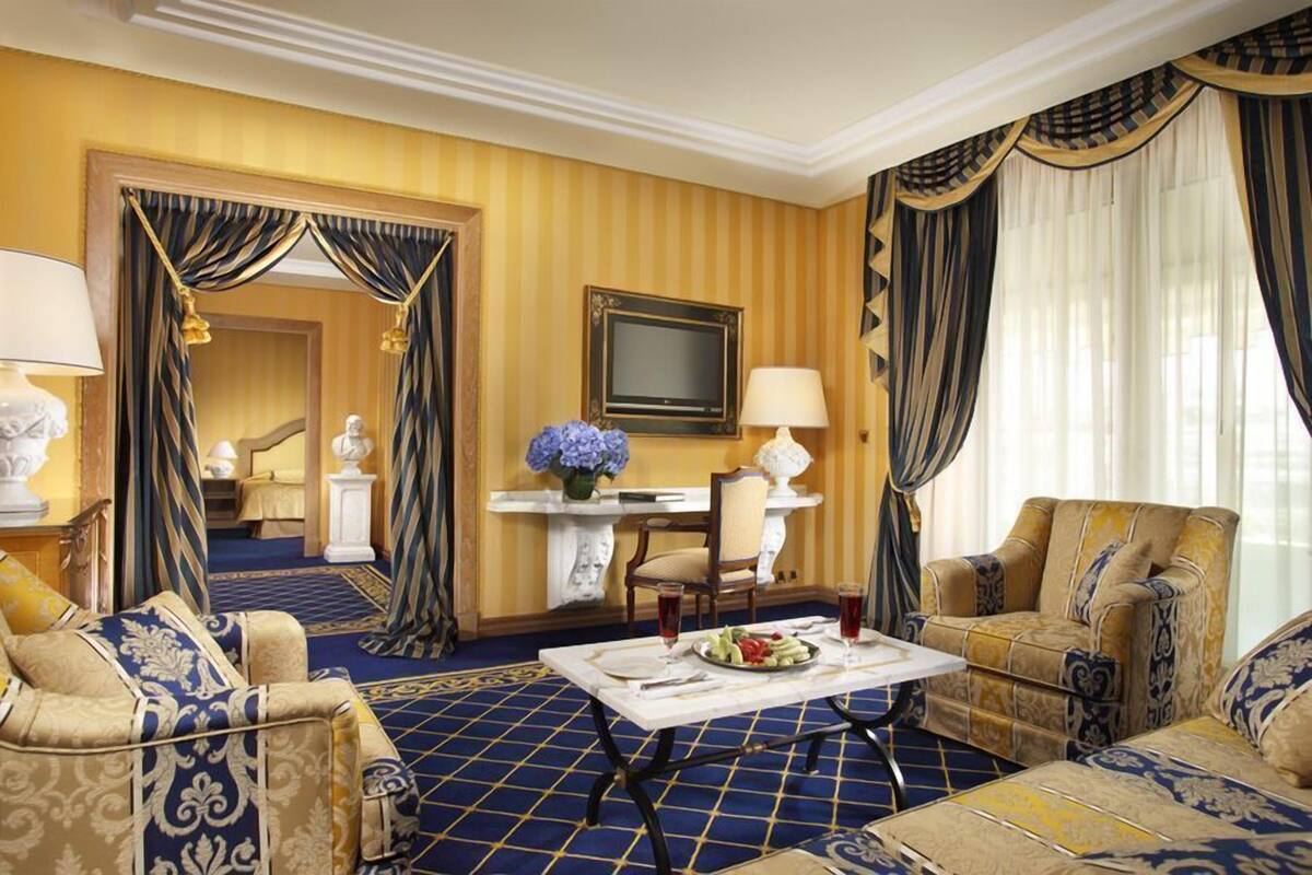 Camera d'albergo con arredamento in tonalità blu e oro, che include una poltrona, una sedia, un tavolo da pranzo e una televisione.