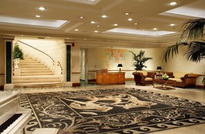 A spacious lobby with a grand staircase, a piano, a patterned carpet, and a seating area with sofas and a coffee table. - Royal Olympic Hotel (Athens)