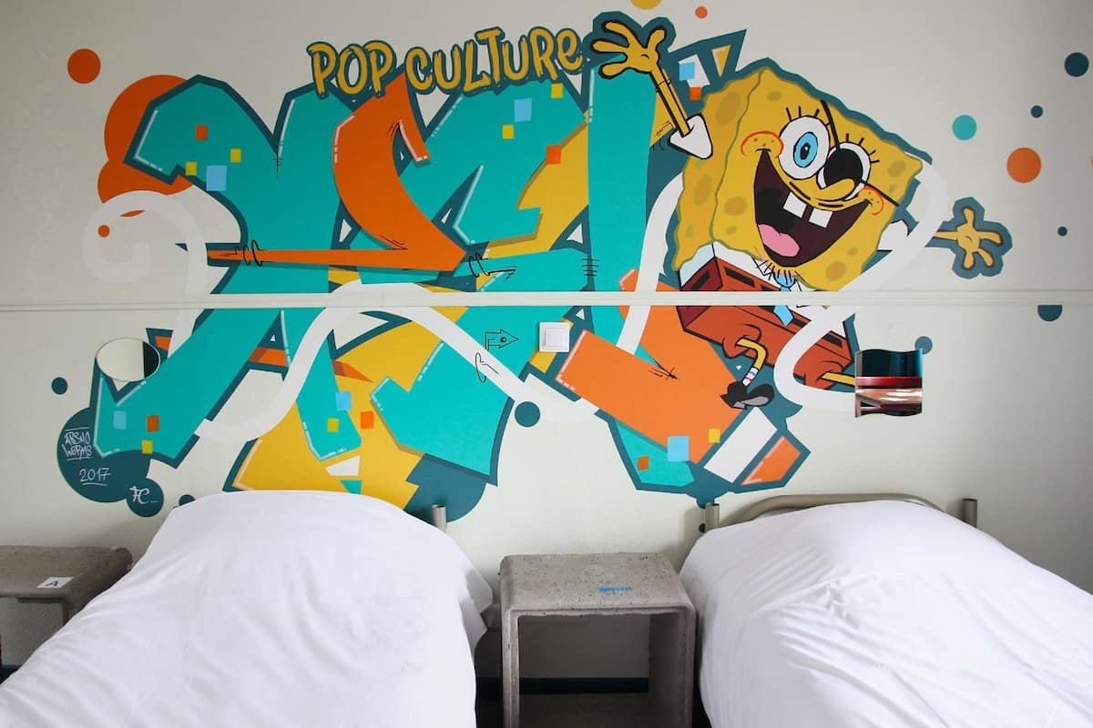 Une chambre d’hôtel avec un mur décoré de graffitis colorés, un lit et une table de chevet.
