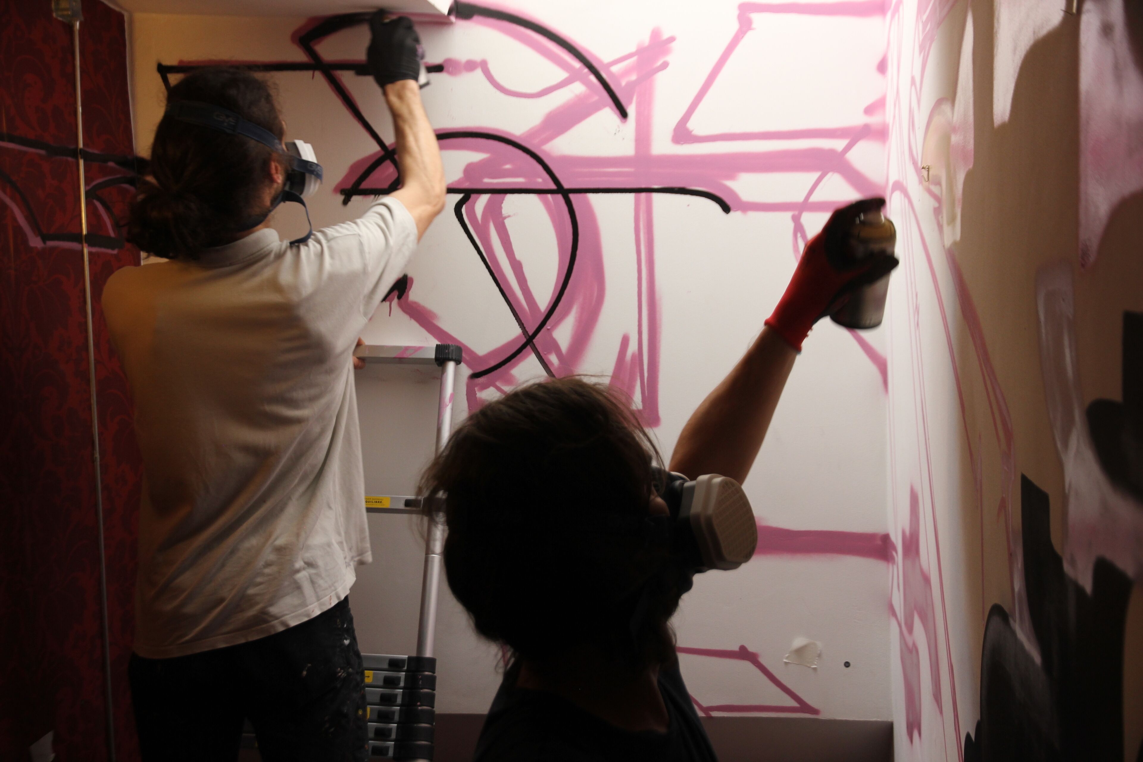 Une personne est en train de peindre un mur avec des graffitis roses.
