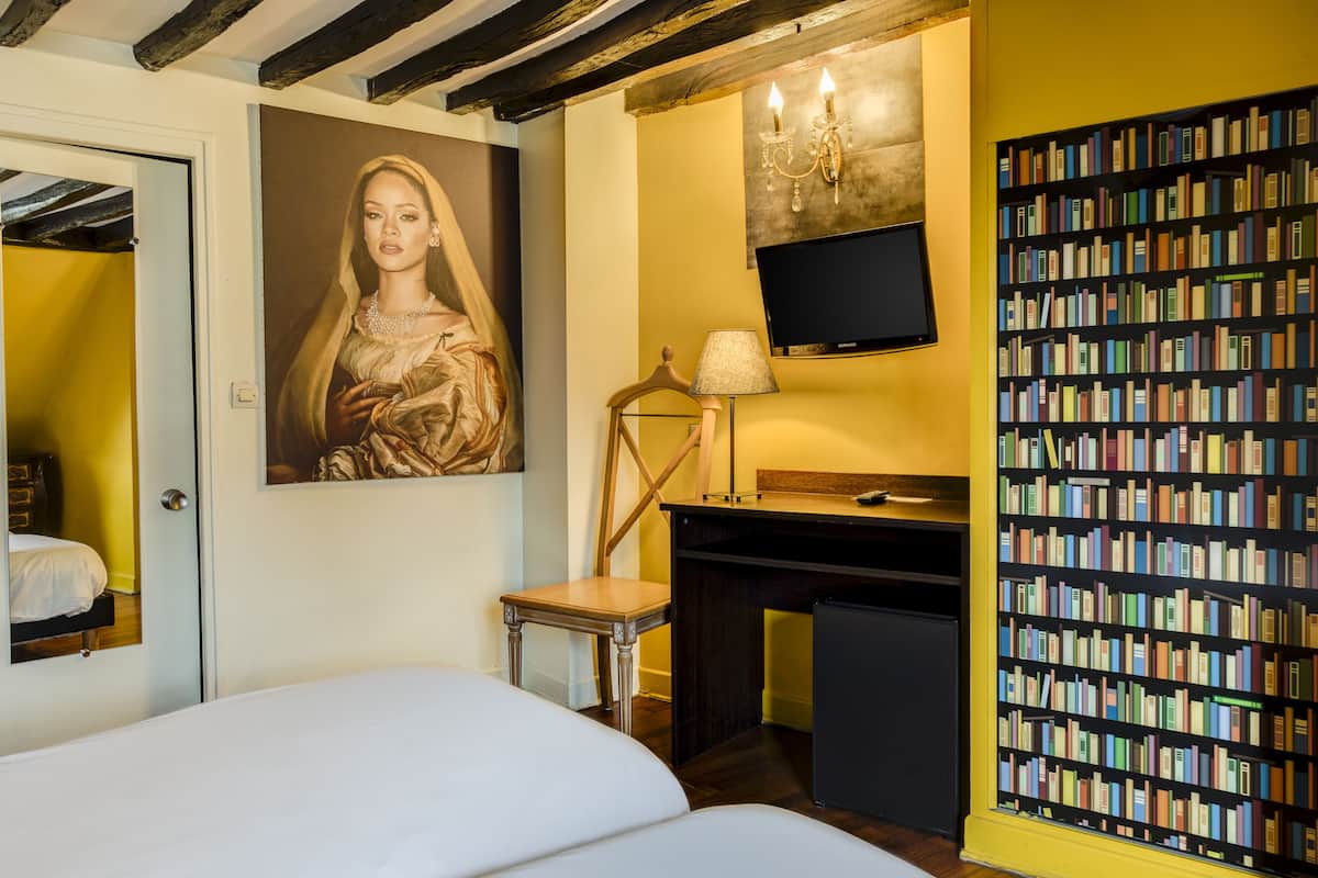 Une chambre d’hôtel avec un lit, un bureau, une bibliothèque, un tableau et un téléviseur.