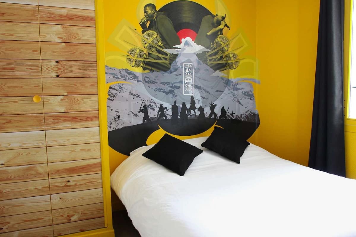 Une chambre d’hôtel avec un lit, un mur lambrissé en bois et une grande affiche représentant une montagne et des personnes.